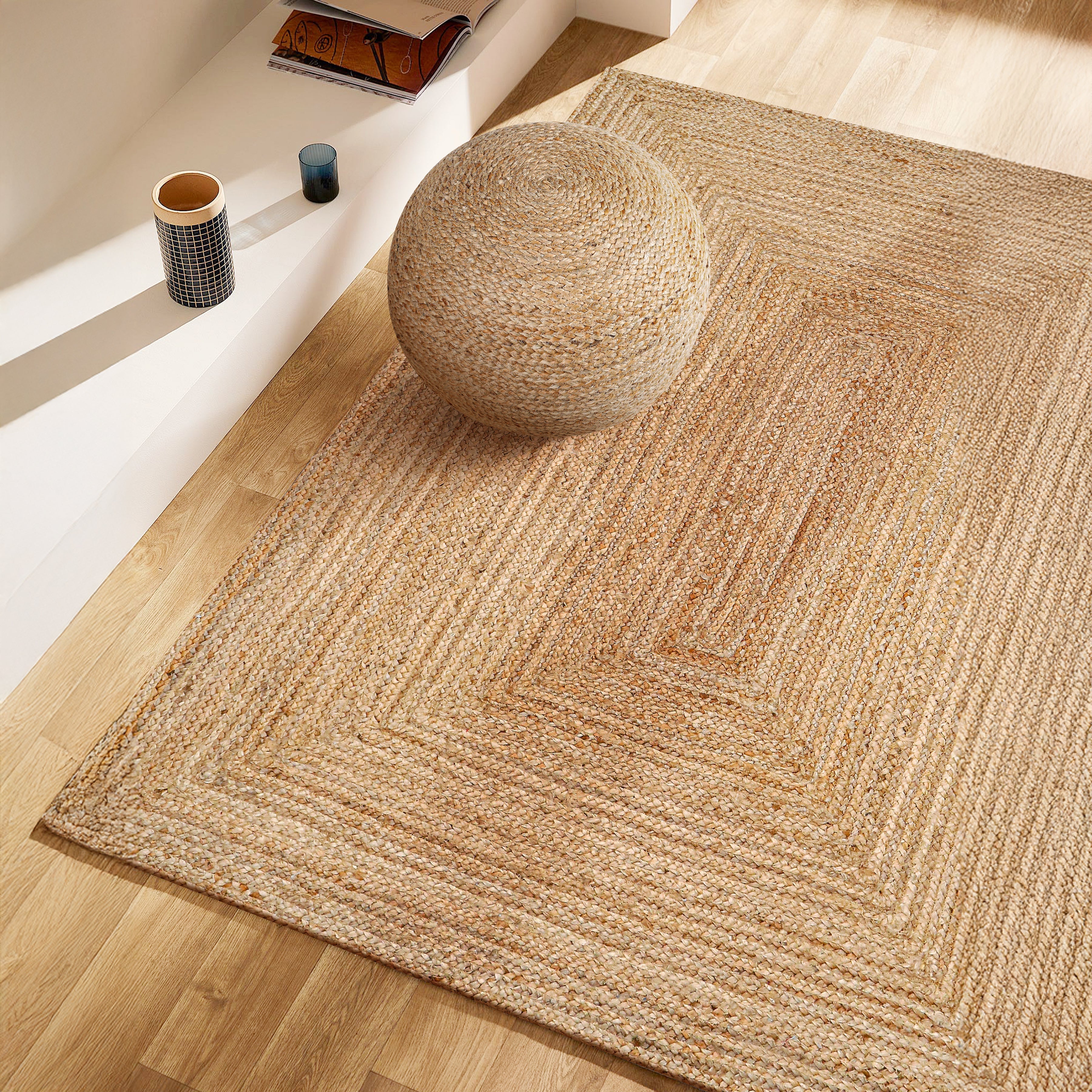 Beige jute rug on a wooden floor with a woven stool in the center.