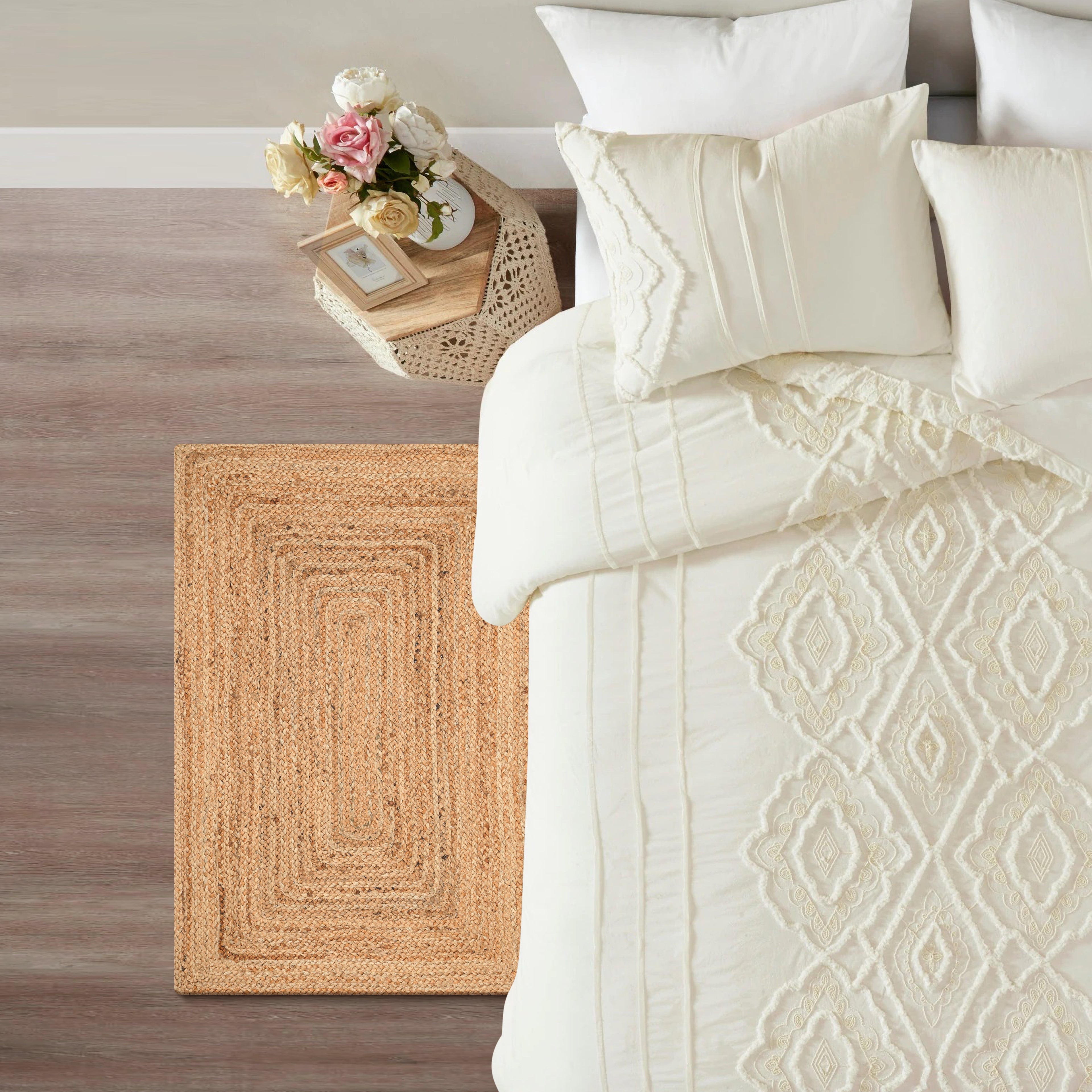 Neatly made bed with white bedding and decorative pillows, next to a woven basket with flowers on a wooden floor.